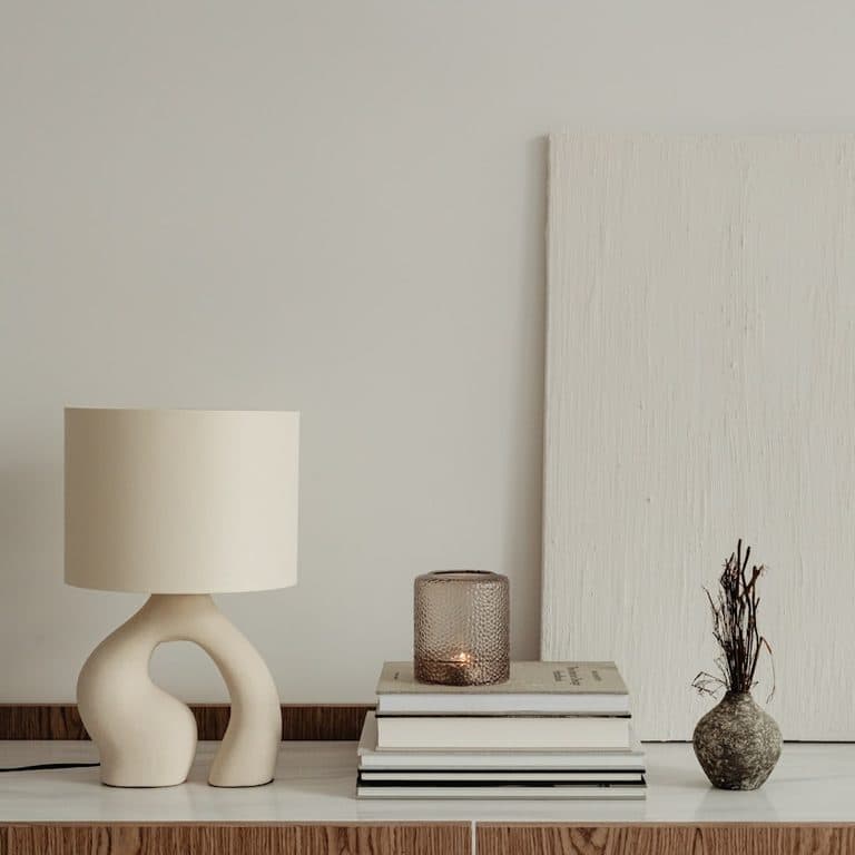 Sculptural ceramic table lamp, a stack of books and a ribbed glass votive on a travertine console