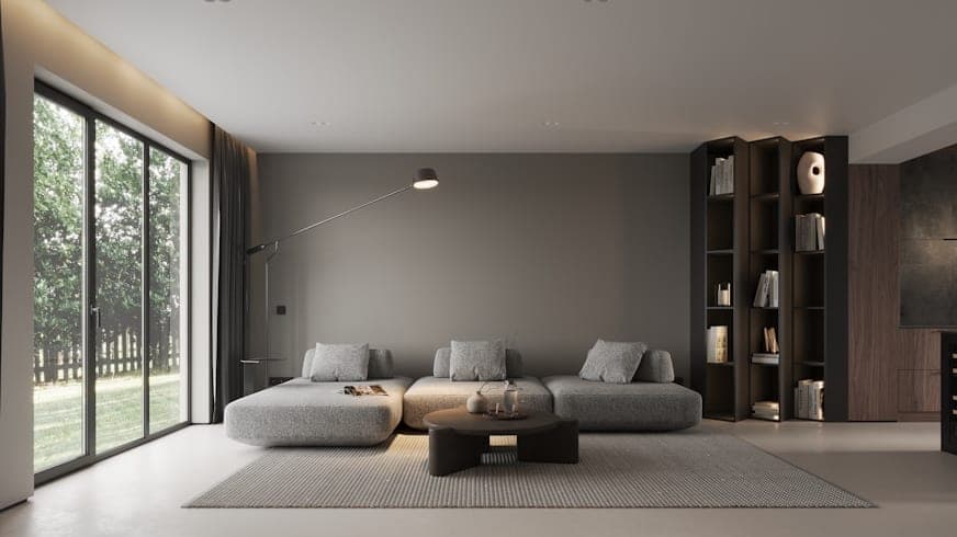 Grey-toned living room with a low modular sofa, an arc lamp and full-height garden glazing