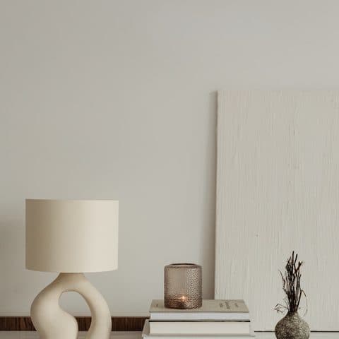Sculptural cream ceramic table lamp with a linen shade, on a travertine console