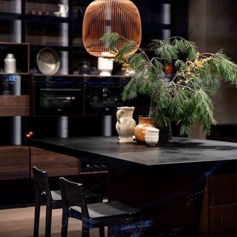 Black stone kitchen island with a copper pendant, clay vessels and a pine branch