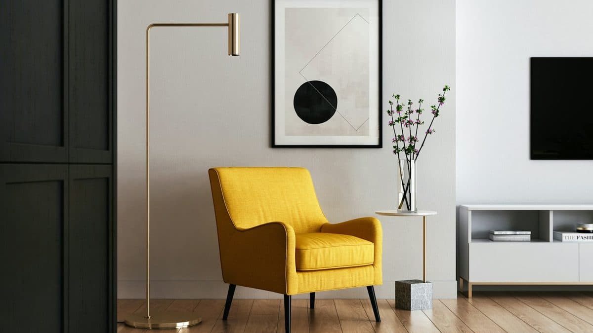 Studio corner with a mustard lounge chair, a brass floor lamp and a framed print above a pale wood floor