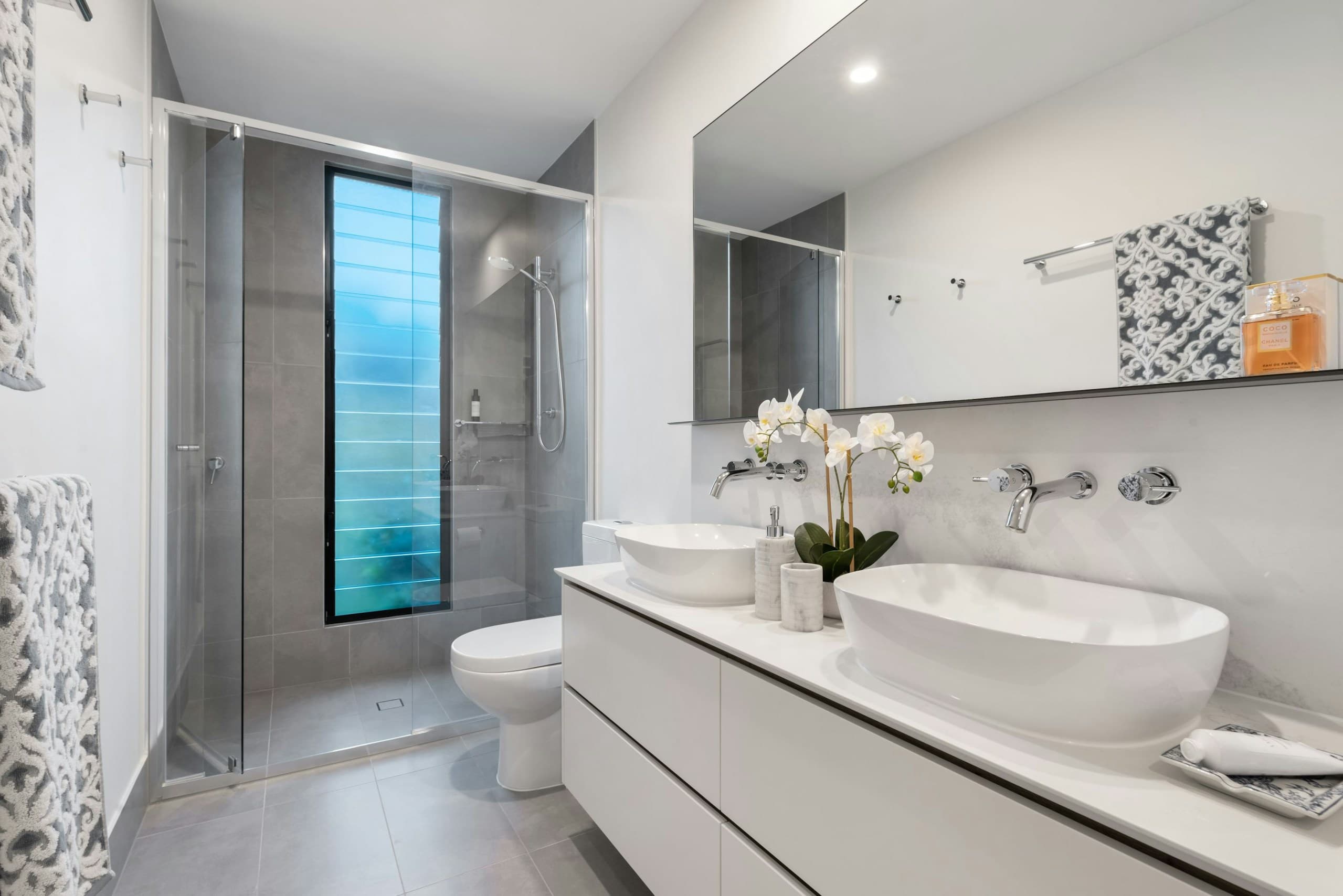 A bathroom showroom with a glass shower, toilet, mirror and twin basins.