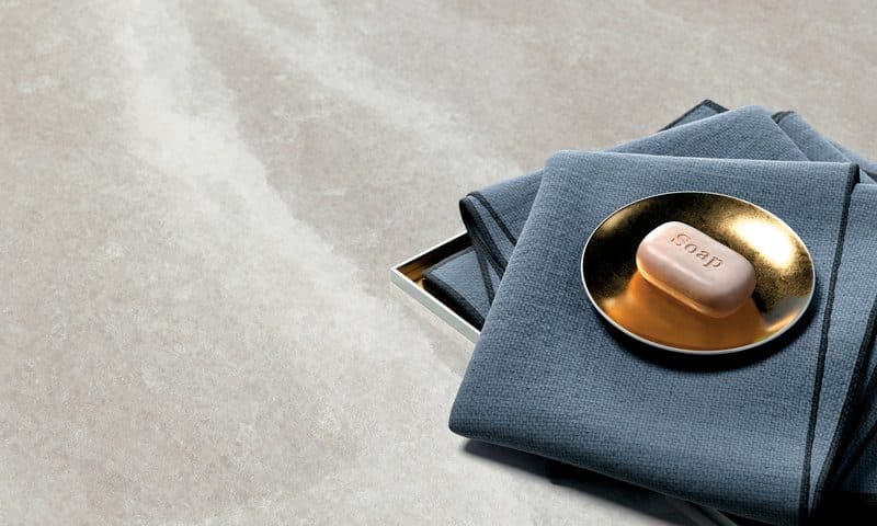 Folded blue-grey linen and a brass dish holding a soap bar on a pale marble surface