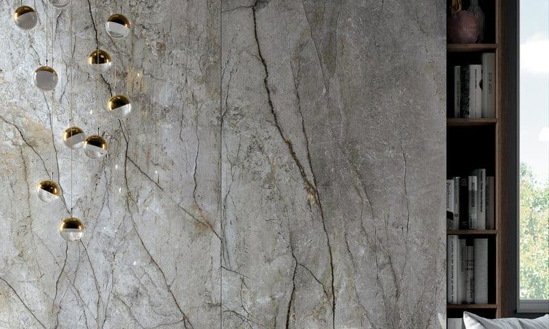 Grey veined marble wall with brass reading lights, beside a filled bookshelf and a window