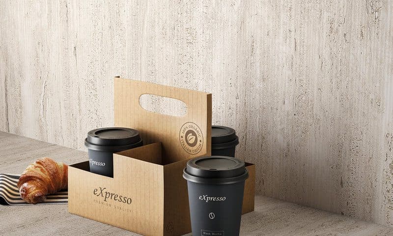 Two takeaway coffee cups in a kraft carrier and a croissant against a vein-cut travertine wall