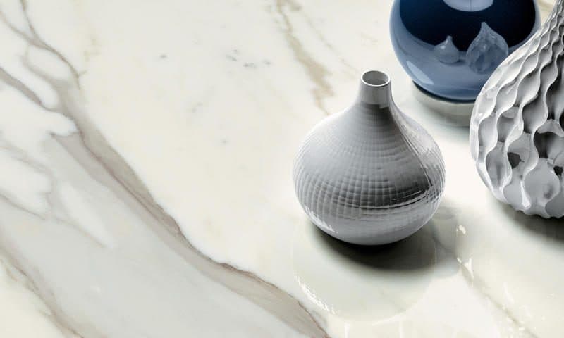 White ceramic bottle vase and two faceted blue-grey vessels on a Calacatta marble top