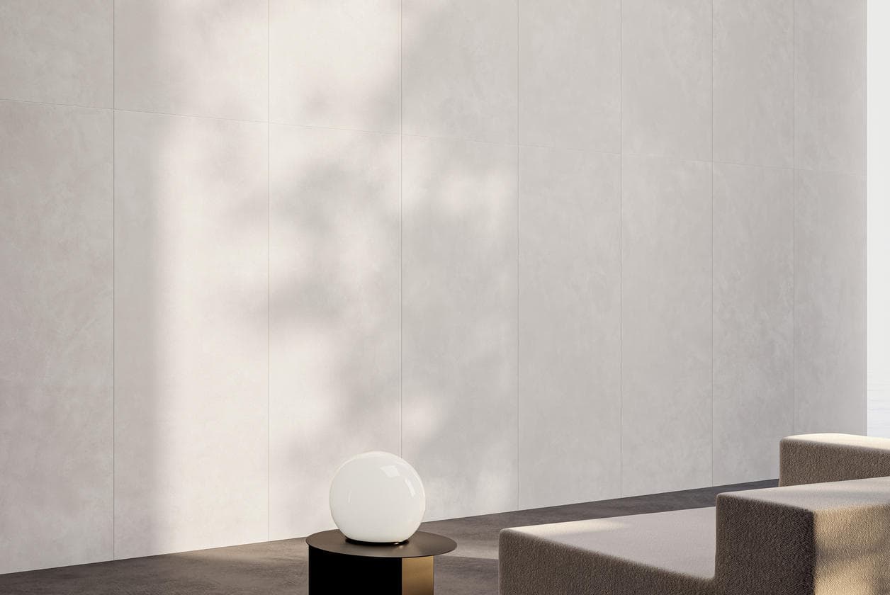 Softly lit corner clad in near-solid neutral large-format slabs, with a spherical floor lamp