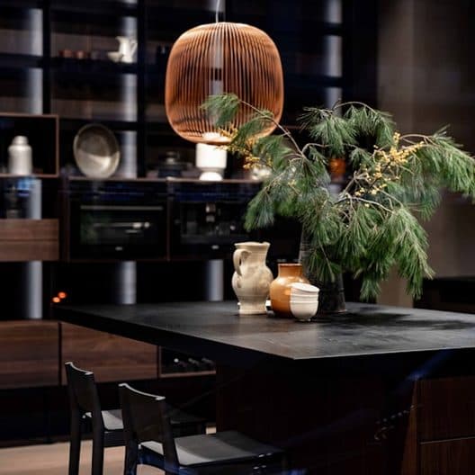 Dark kitchen with a black stone island, a copper pendant and clay vessels