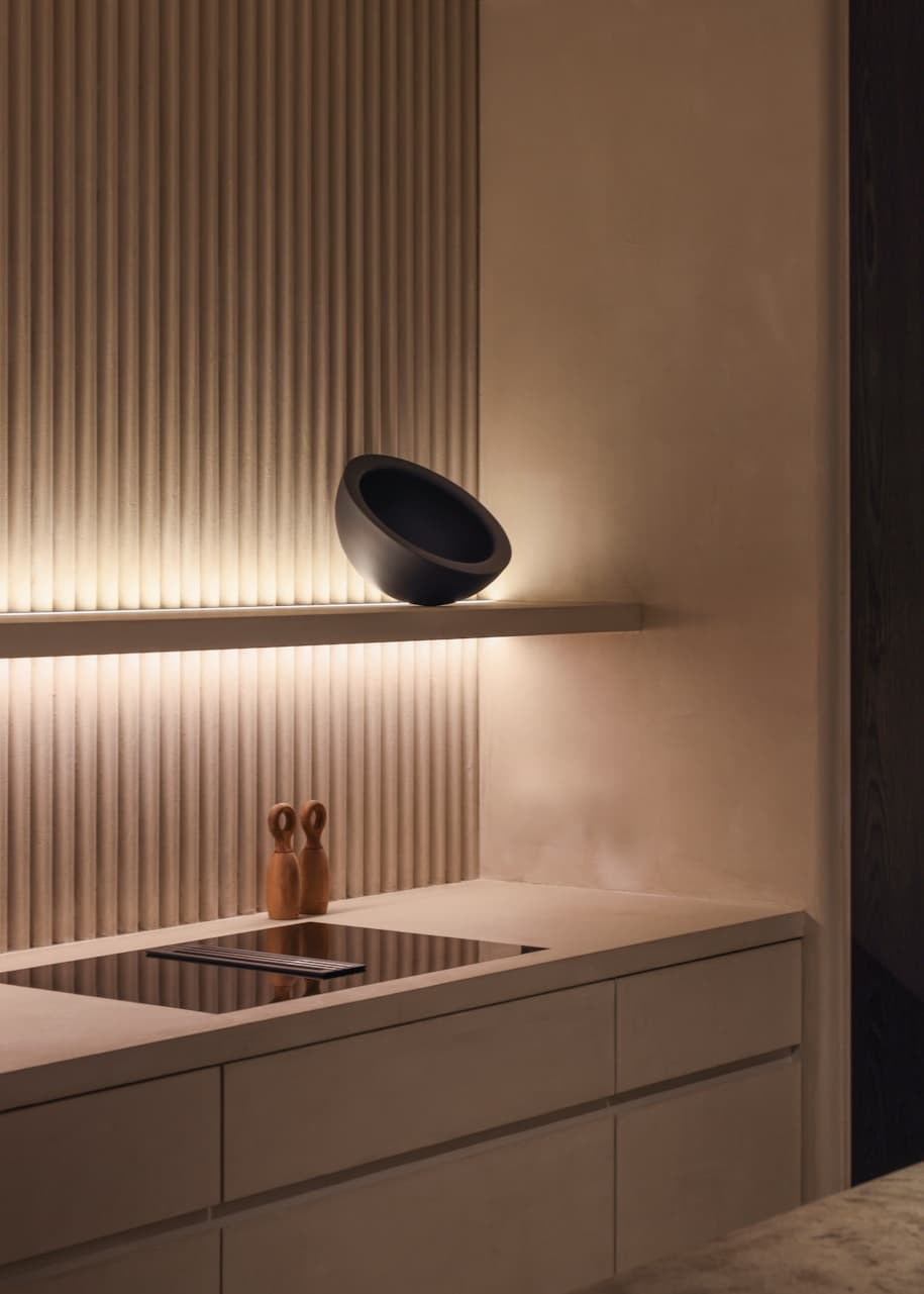 Warm beige kitchen with a fluted wall, backlit shelf and induction cooktop