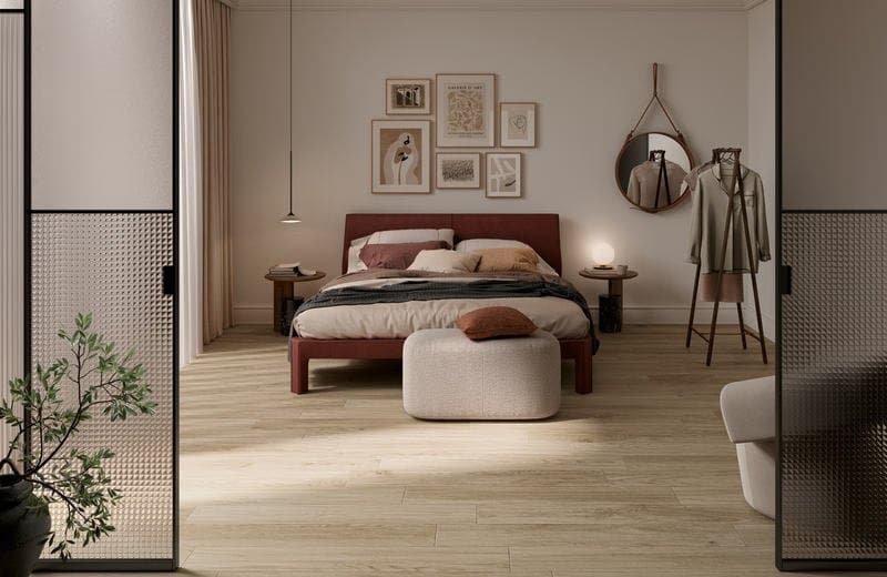 Bedroom seen through a glazed sliding door, with a rust upholstered bed, a framed print wall and pale wood-effect flooring