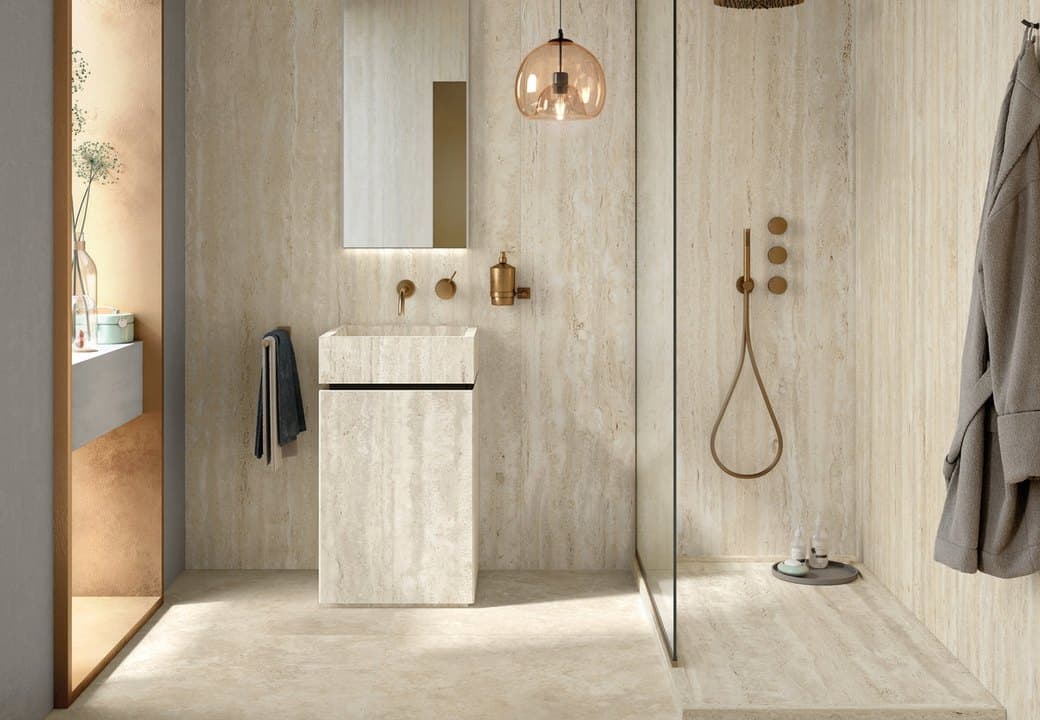 Travertine bathroom with a monolithic stone basin, brushed brass wall taps and mixer, a glass-screened shower and a hanging robe
