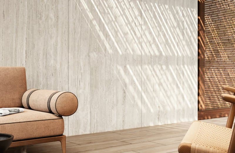 Shaded terrace with a travertine wall striped by light through a timber screen, a linen armchair and wood-effect decking